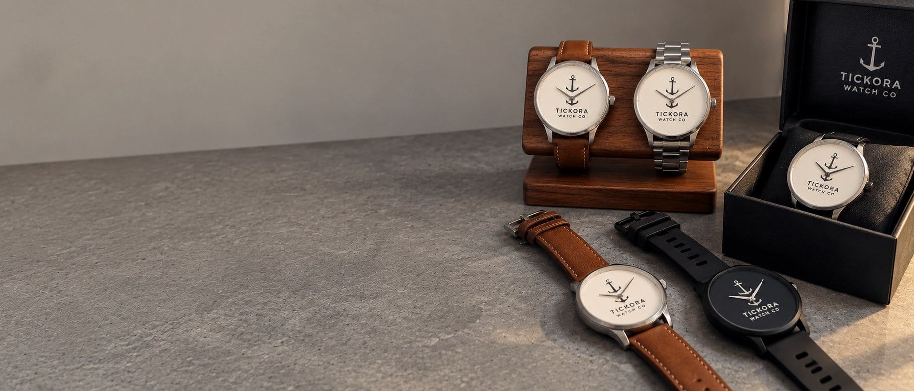 Custom logo watches with plain dials on a walnut stand, lying flat and in an open gift box on a grey countertop